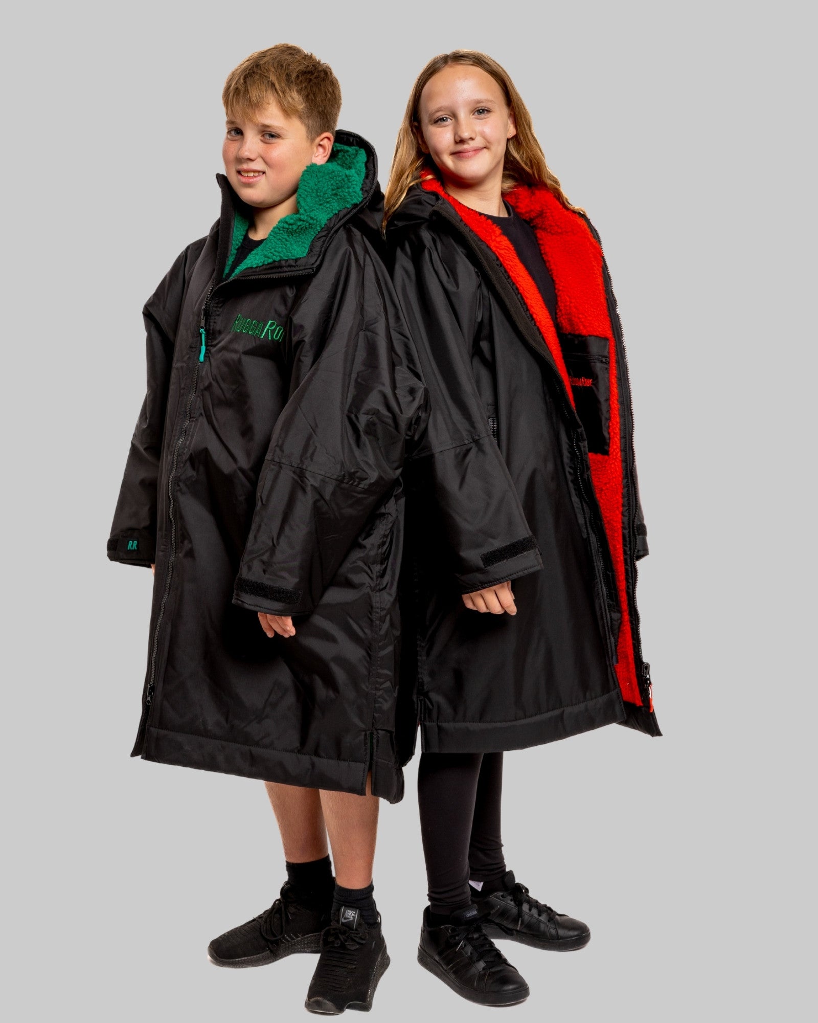 Two children wearing black with green and red interior accents on a gray background