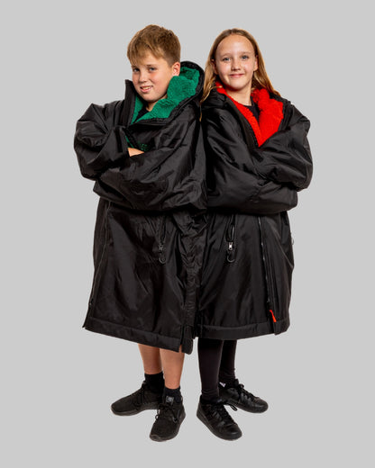 Two children wearing black with green and red interior accents on a gray background