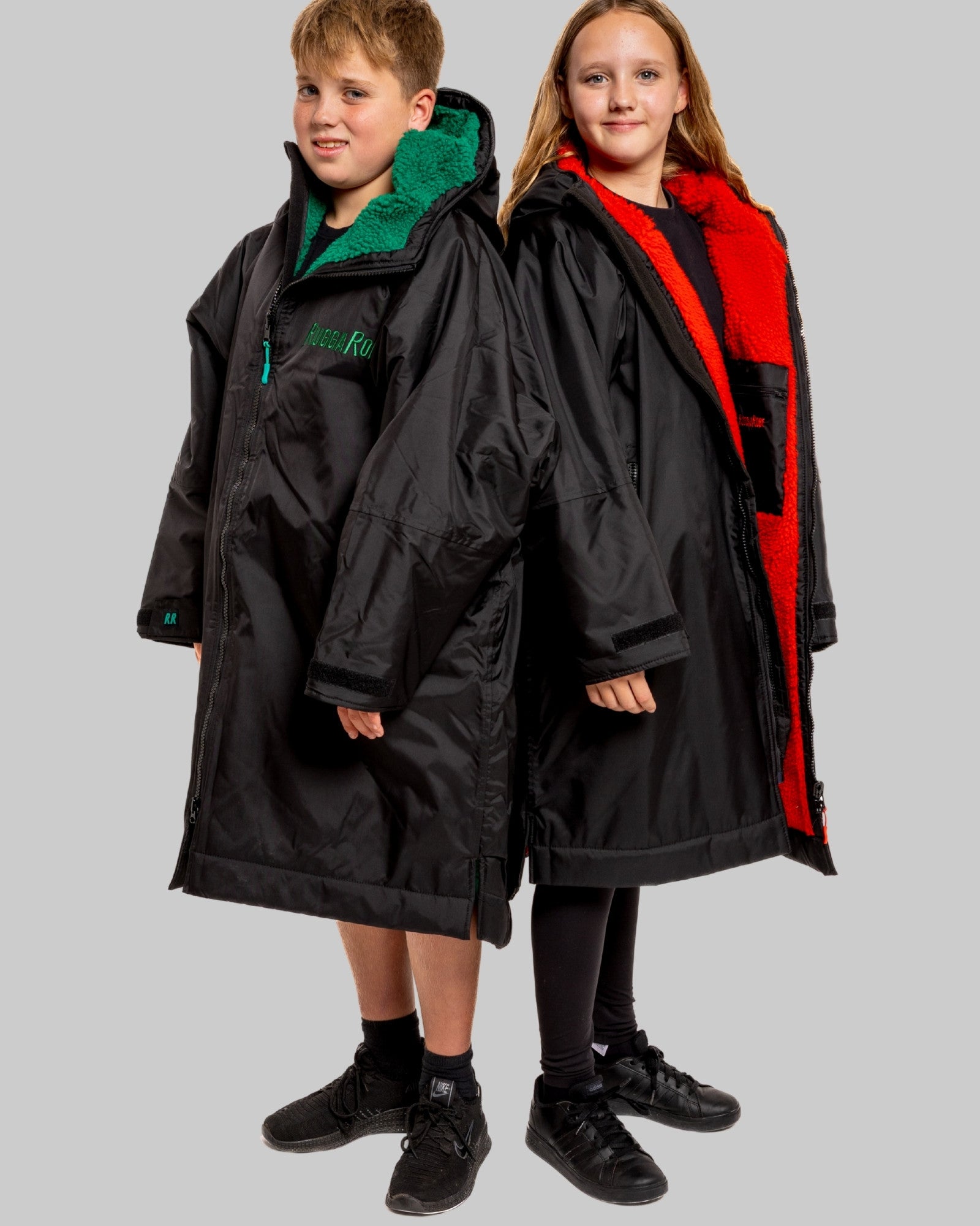 Two children wearing black with green and red interior accents on a gray background