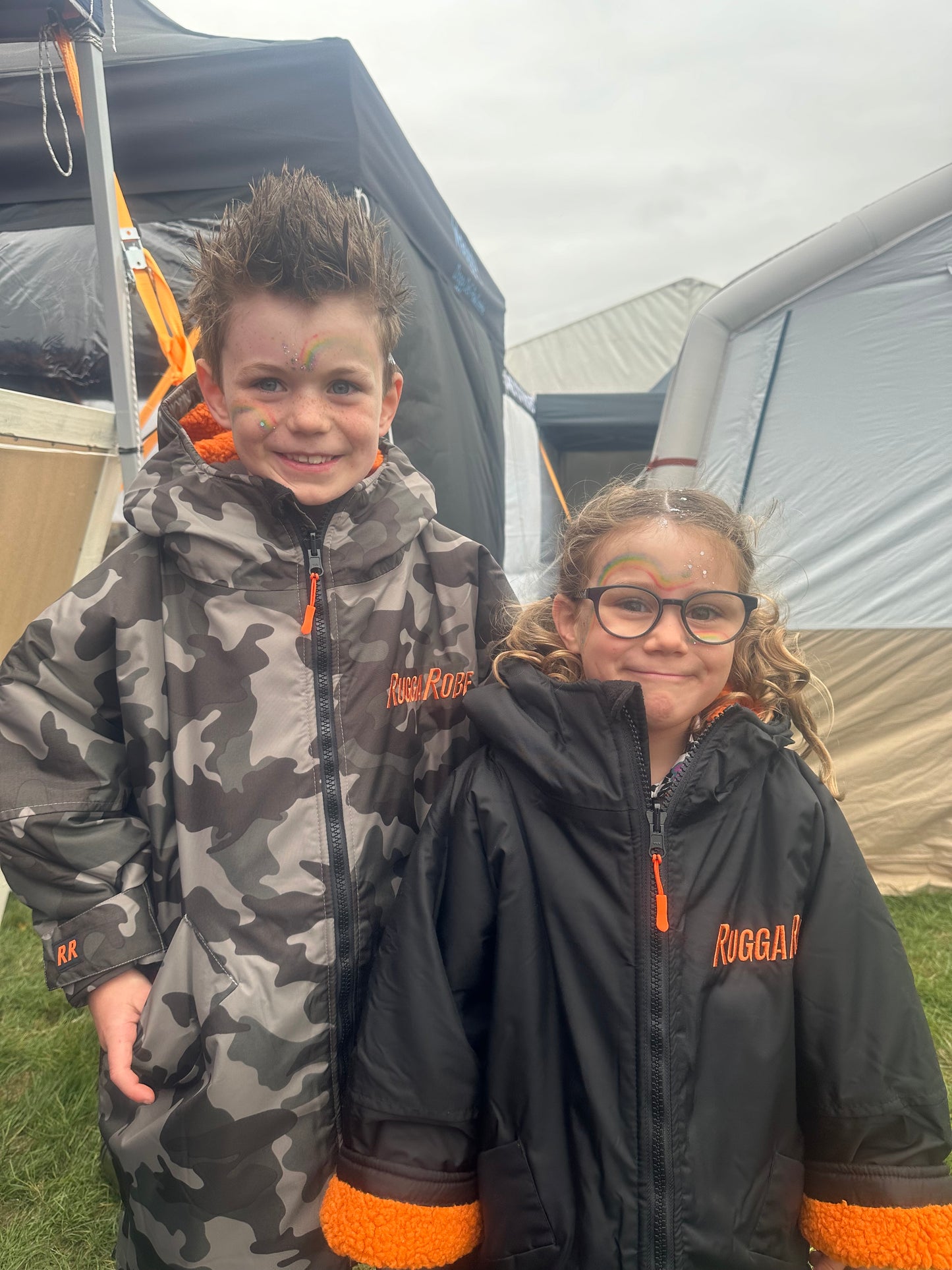 Two people wearing RuggaRobe changerobes with orange accents standing in front of a tent.