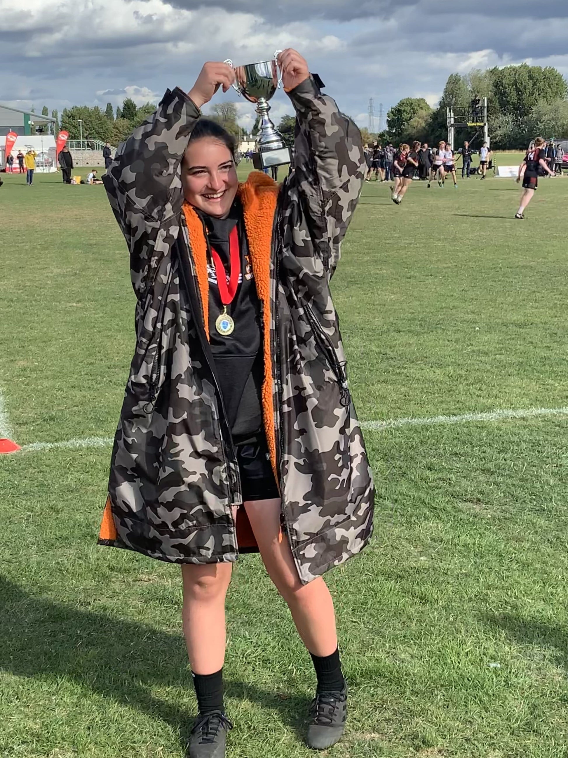 Person wearing RuggaRobe grey camo change robe with orange fleece interior on a sports field
