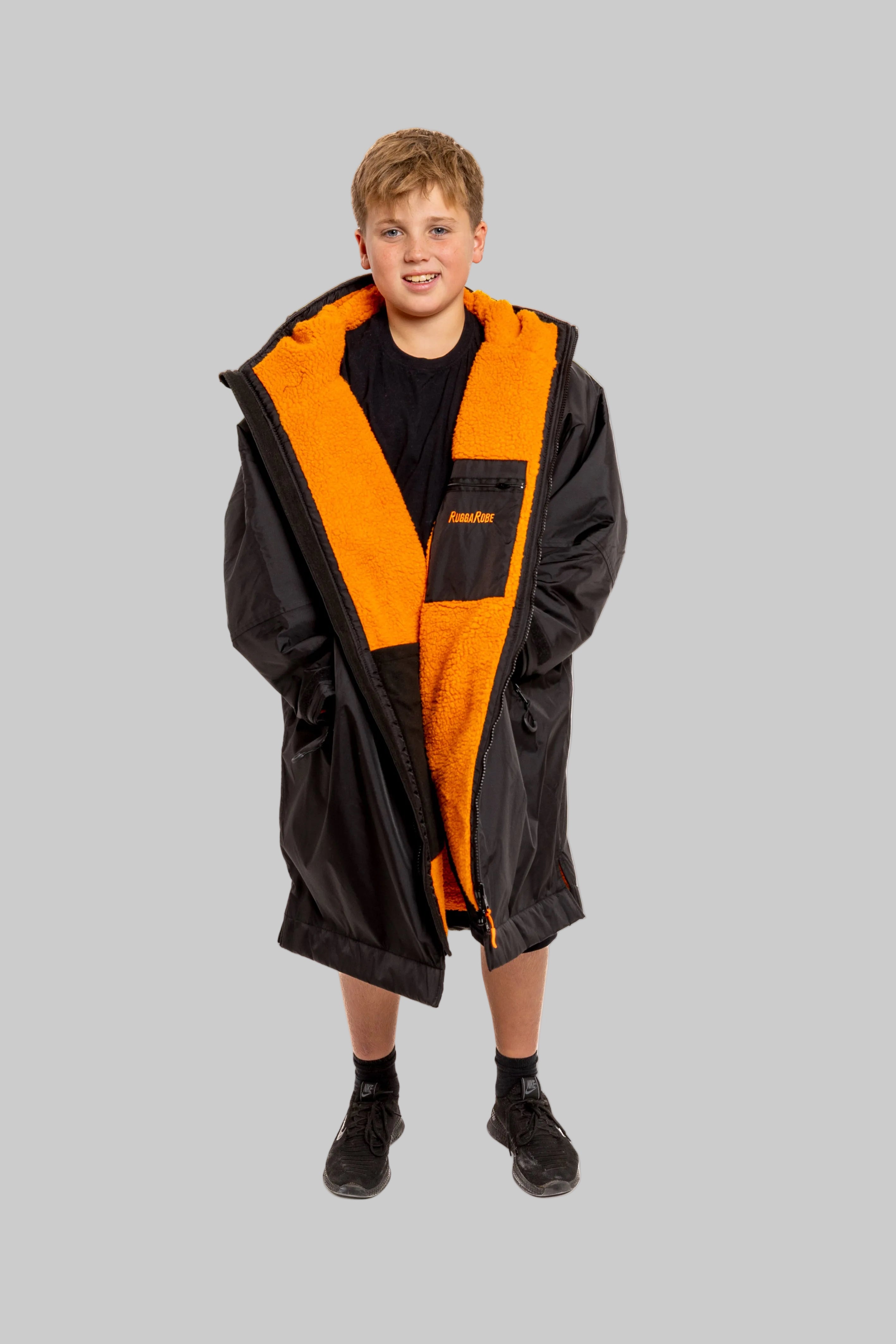 Child wearing RuggaRobe black change robe with orange fleece interior on grey background