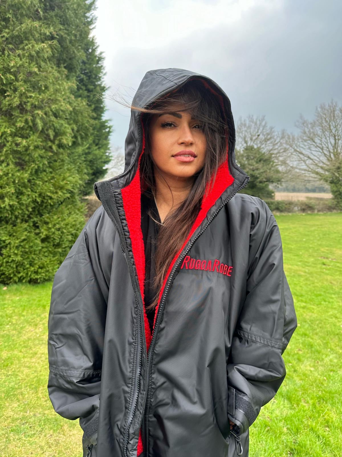 Model wearing RuggaRobe black change robe with red fleece interior in a sportsfield