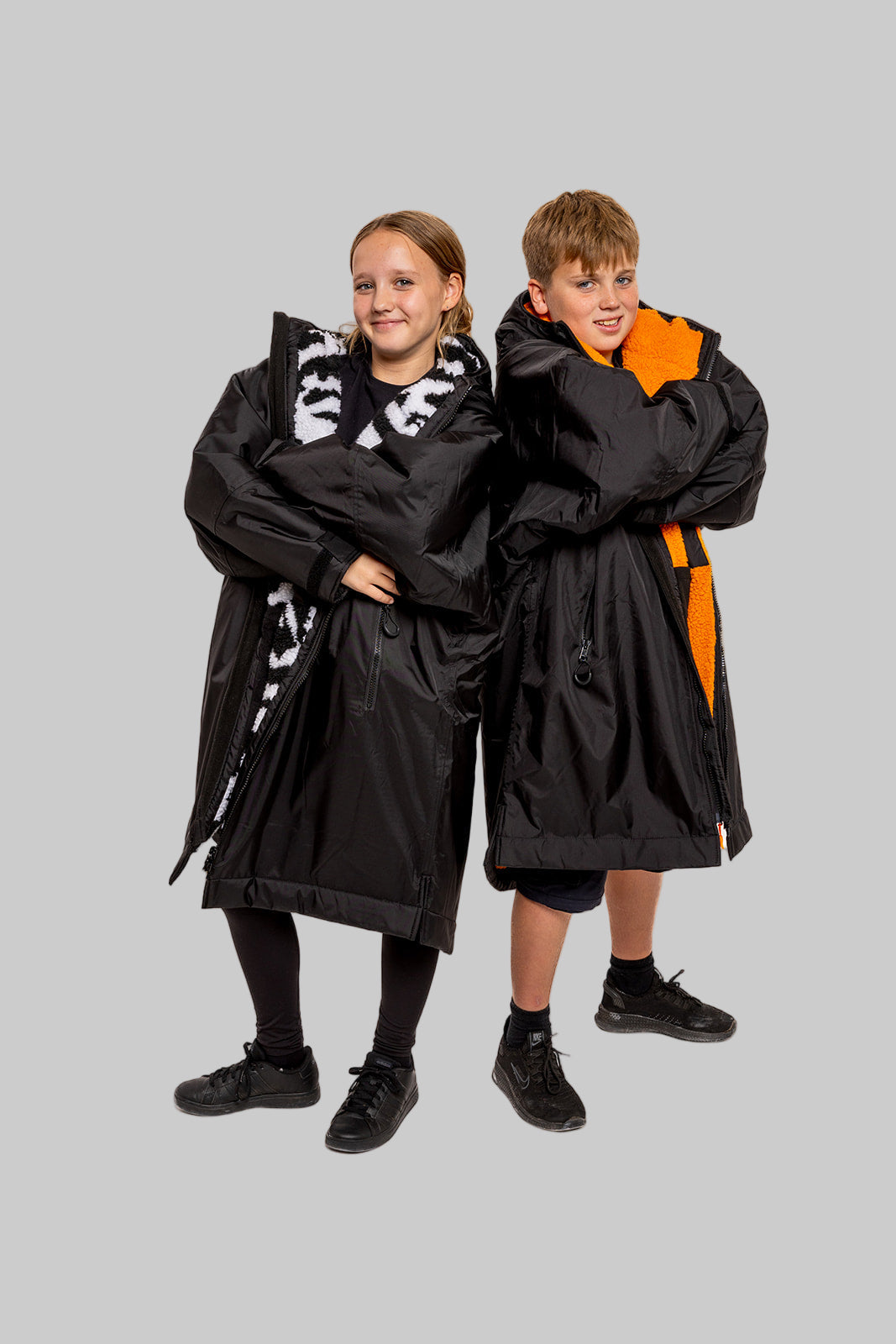 Two people wearing black ruggarobes with orange accents on a gray background