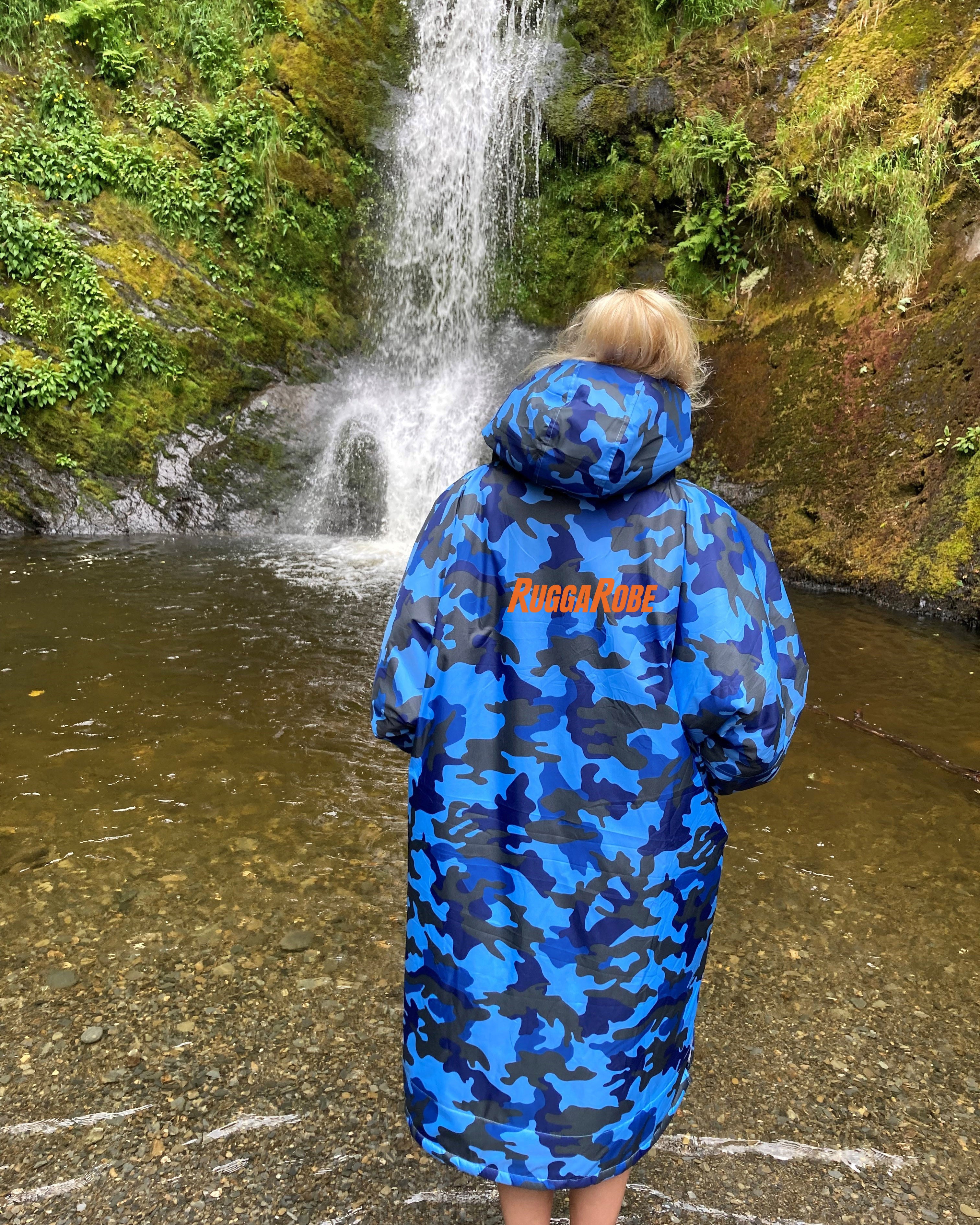 Person wearing a blue camo changerobe on a standing next to a waterfall