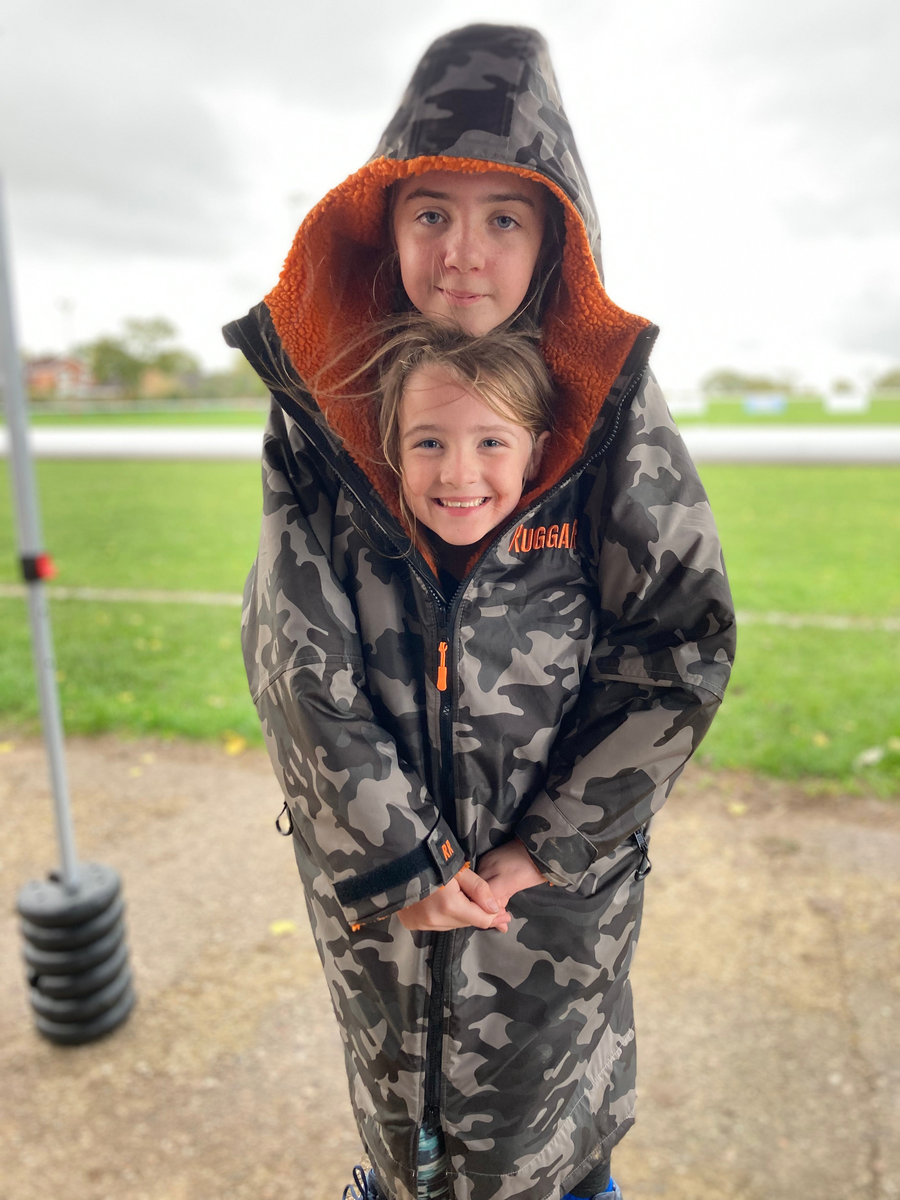 Two children wearing a grey camo change robe with orange fleece lining, standing outdoors.